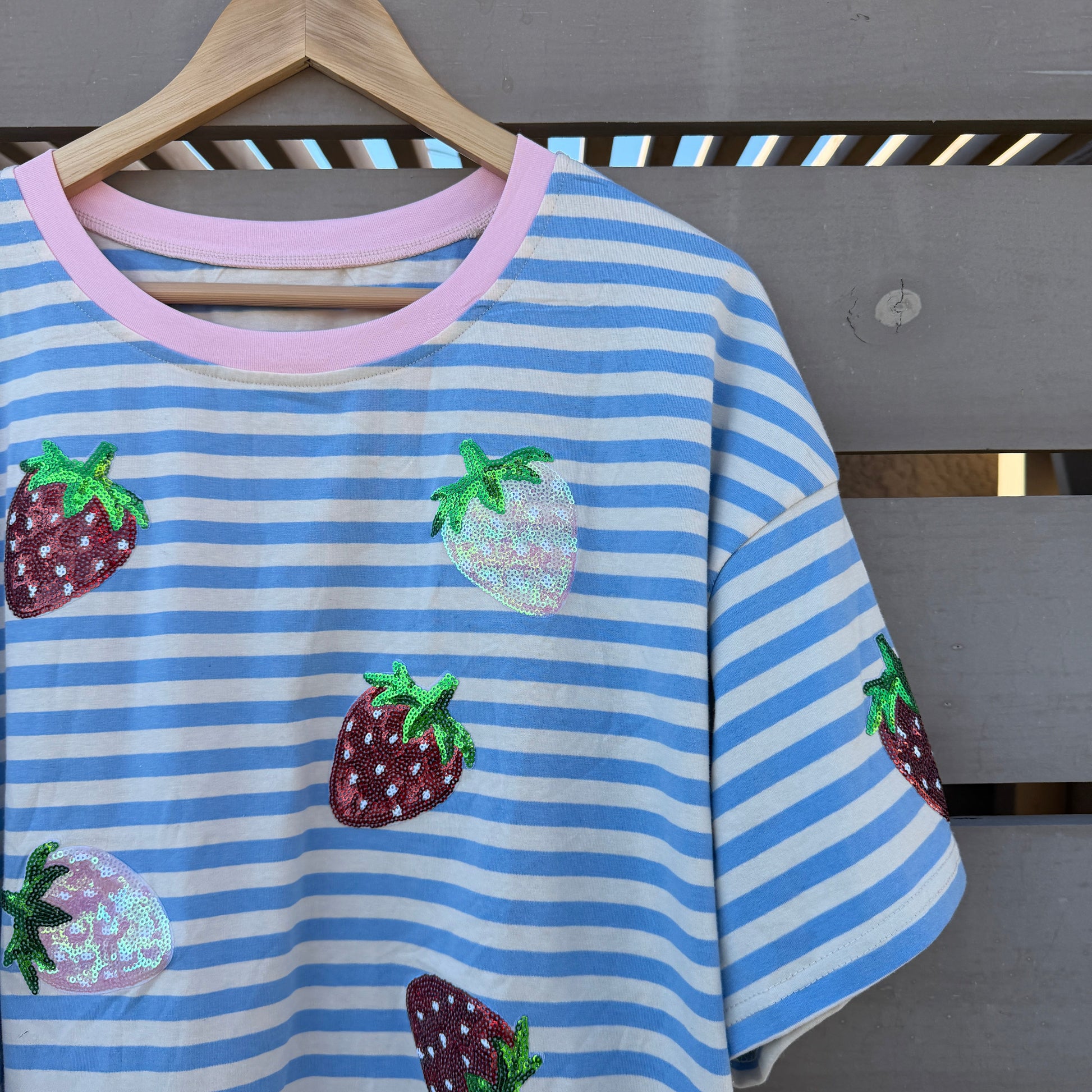 Blue and white striped shirt with strawberry patterns on a wooden hanger against a wooden background