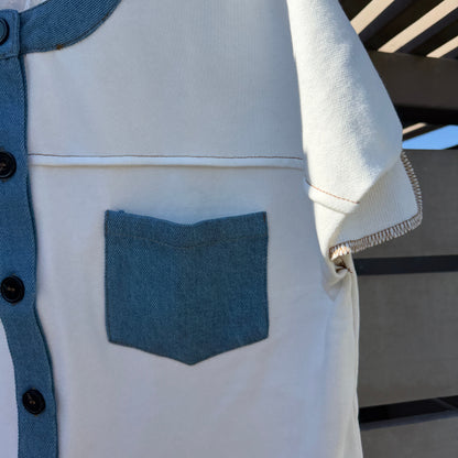 Light-colored shirt with blue accents and a pocket, hanging against a neutral background.
