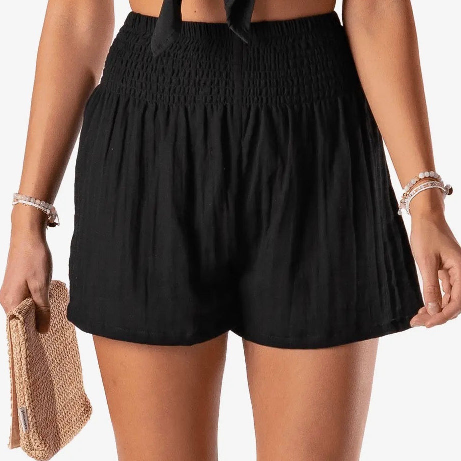 Person wearing black shorts holding a beige clutch against a neutral background