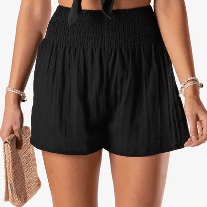 Person wearing black shorts holding a beige clutch against a neutral background