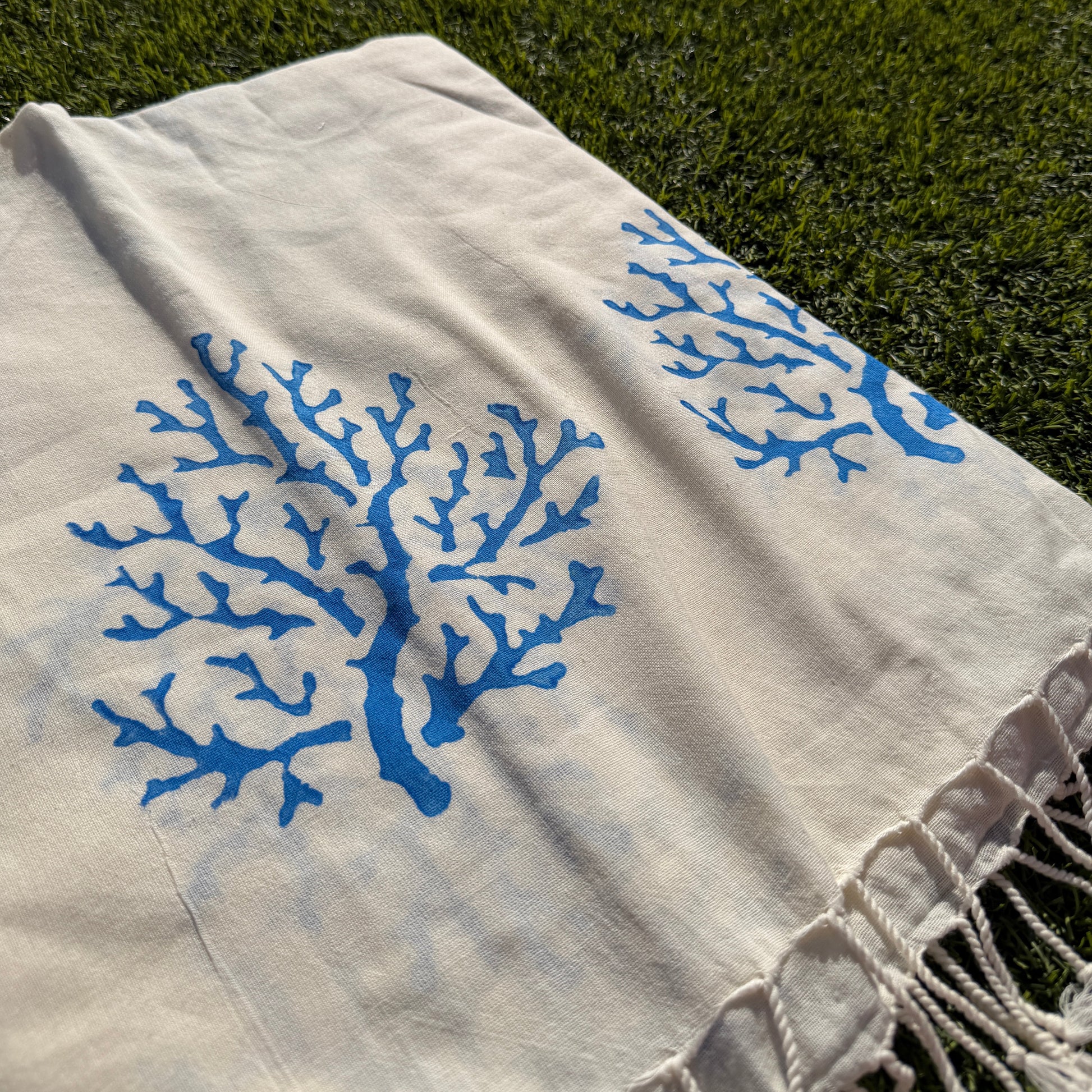 White fabric with blue coral patterns on a green grass background