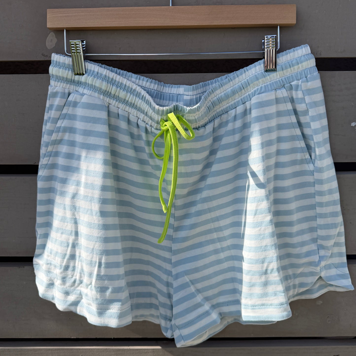 Blue and white striped shorts with a green drawstring on a wooden hanger against a wooden background.