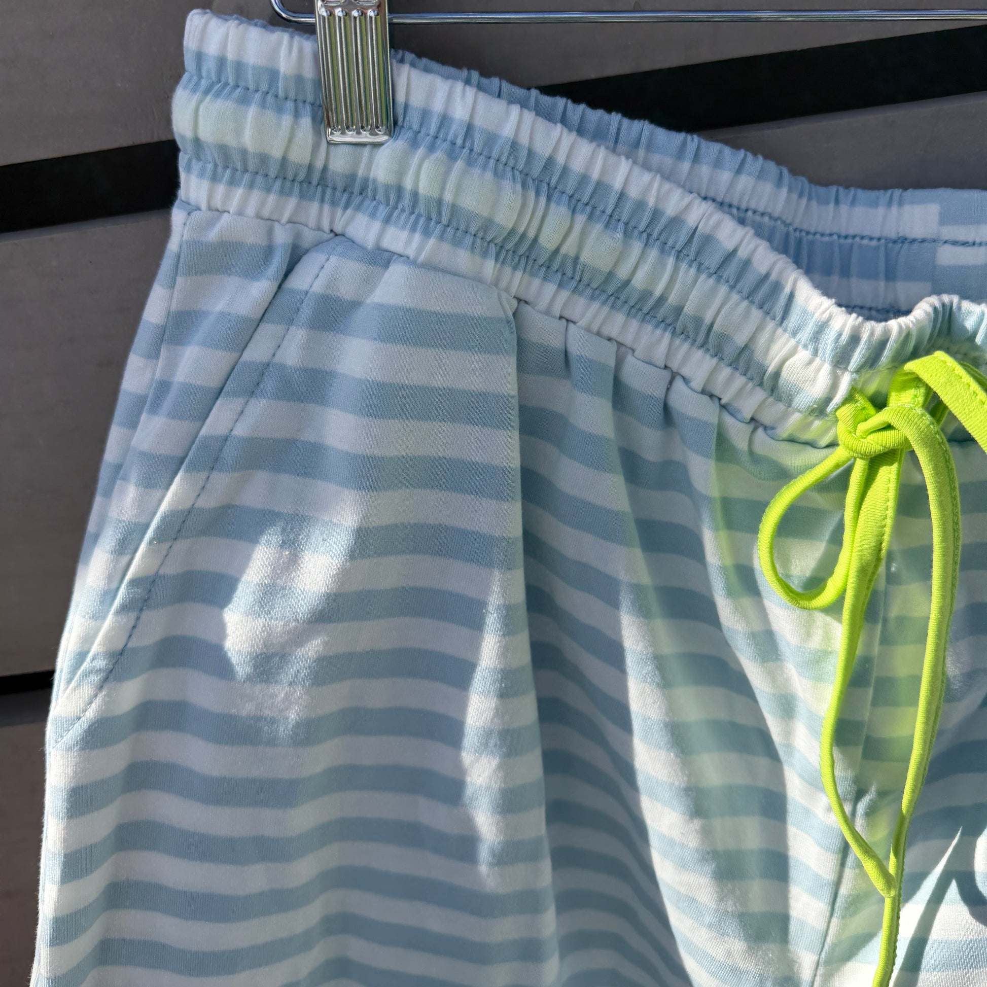 Blue and white striped shorts with a green drawstring hanging on a rack.