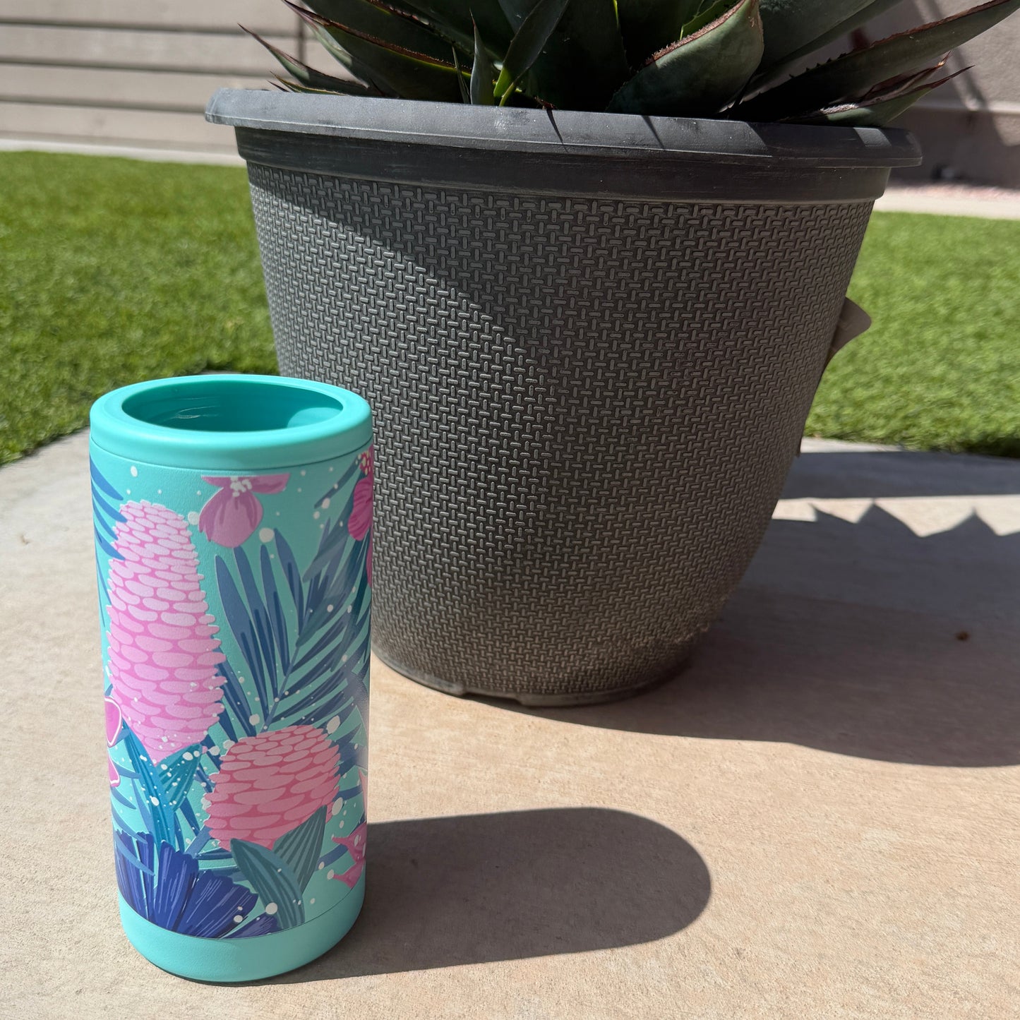 Colorful tumbler with floral design on a concrete surface next to a potted plant.