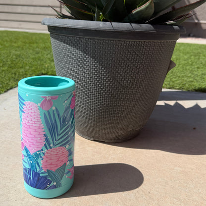 Colorful tumbler with floral design on a concrete surface next to a potted plant.