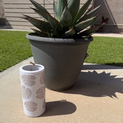 White tumbler with leaf pattern next to a potted plant on a concrete surface.