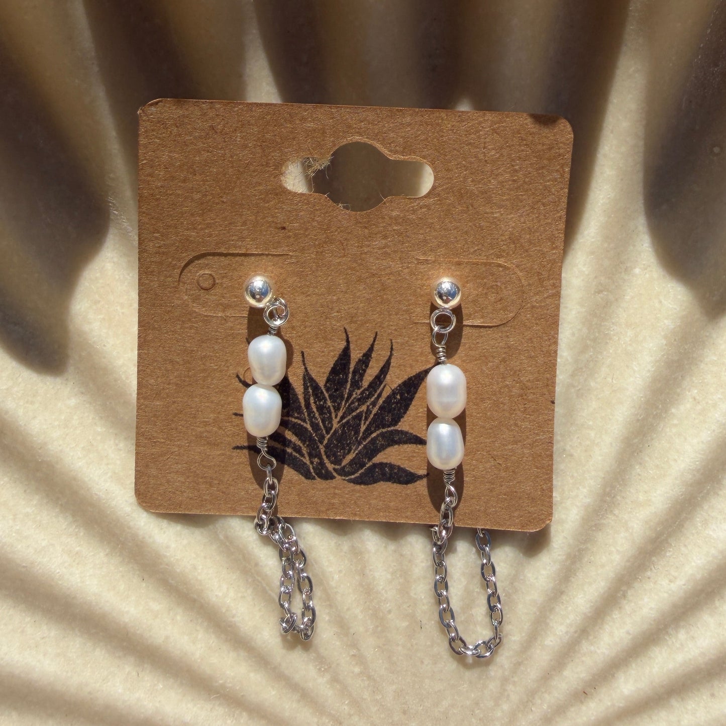 earrings pearls on a cardboard backing against a textured beige background