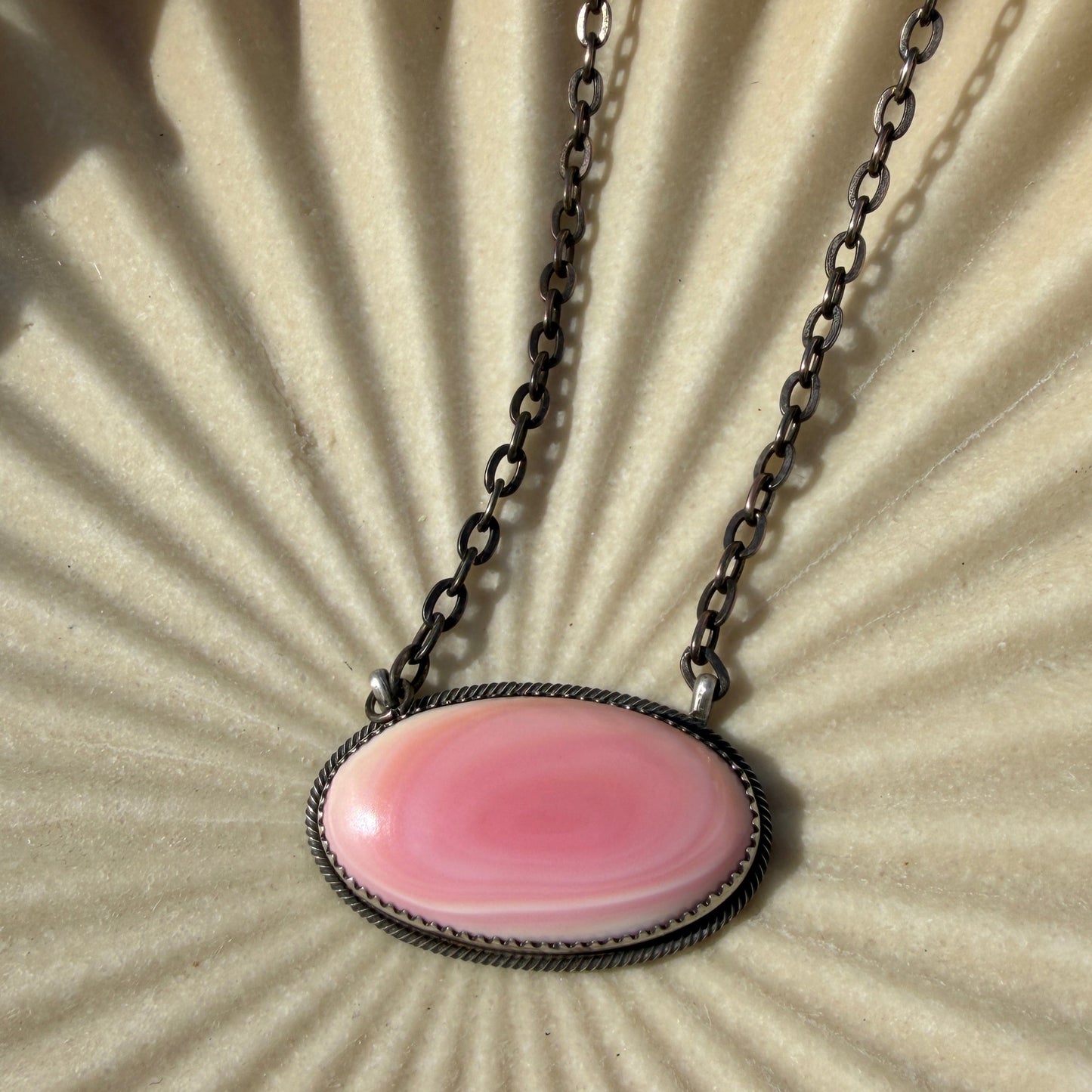 Necklace with a pink pendant on a textured beige background