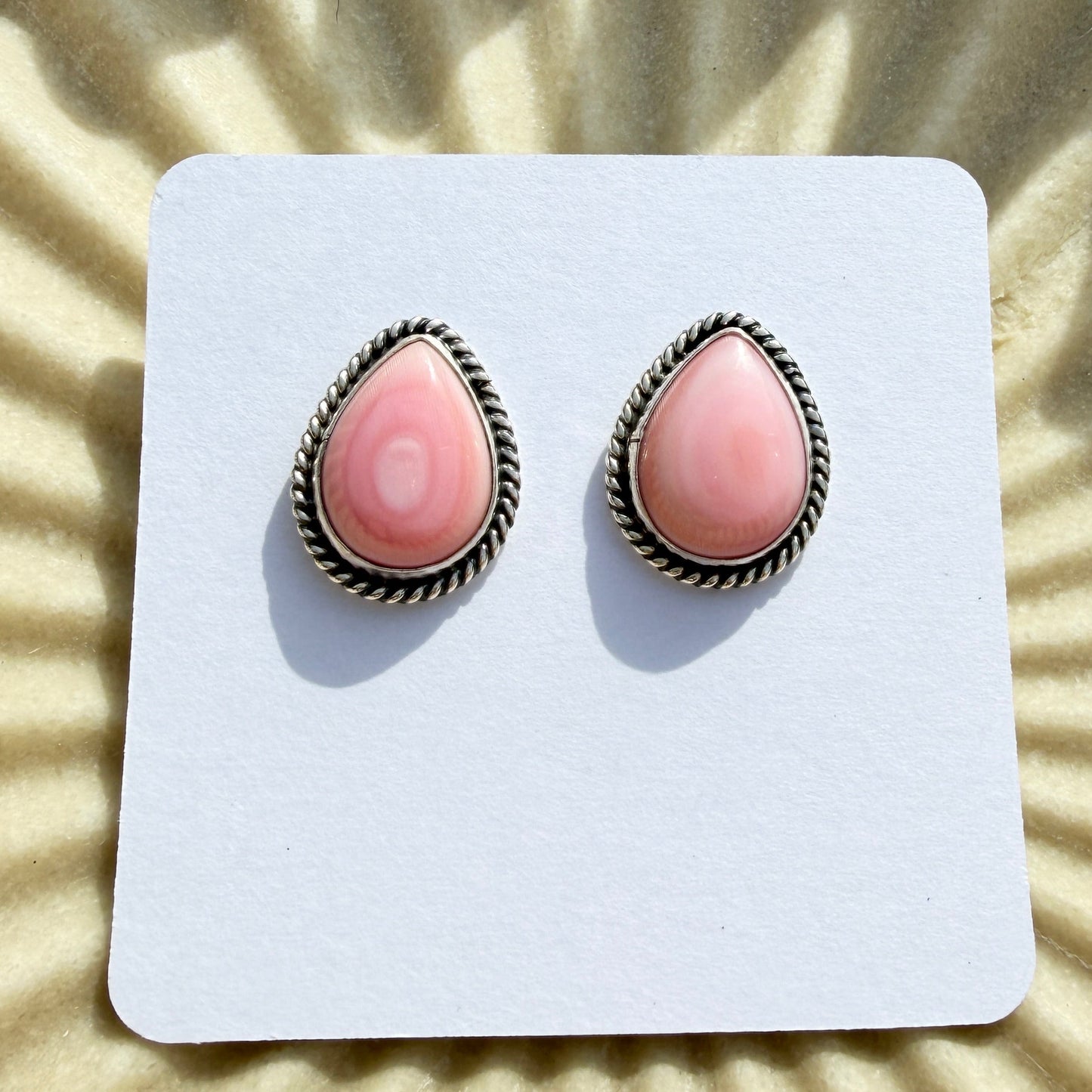 Pair of pink teardrop earrings on a white card with a sunburst background
