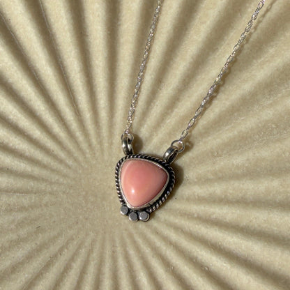 Necklace with a triangle shaped pink pendant on a textured beige surface