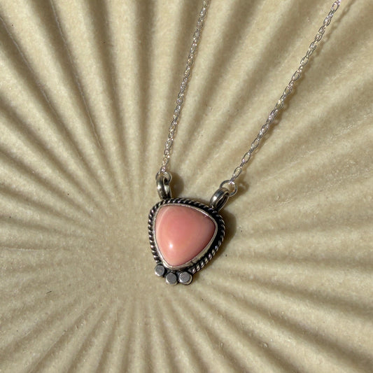 Necklace with a triangle shaped pink pendant on a textured beige surface