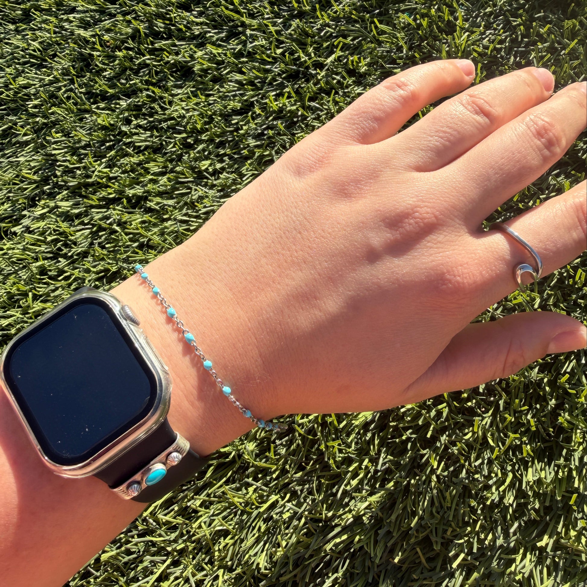 Hand wearing a smartwatch and bracelet on grass