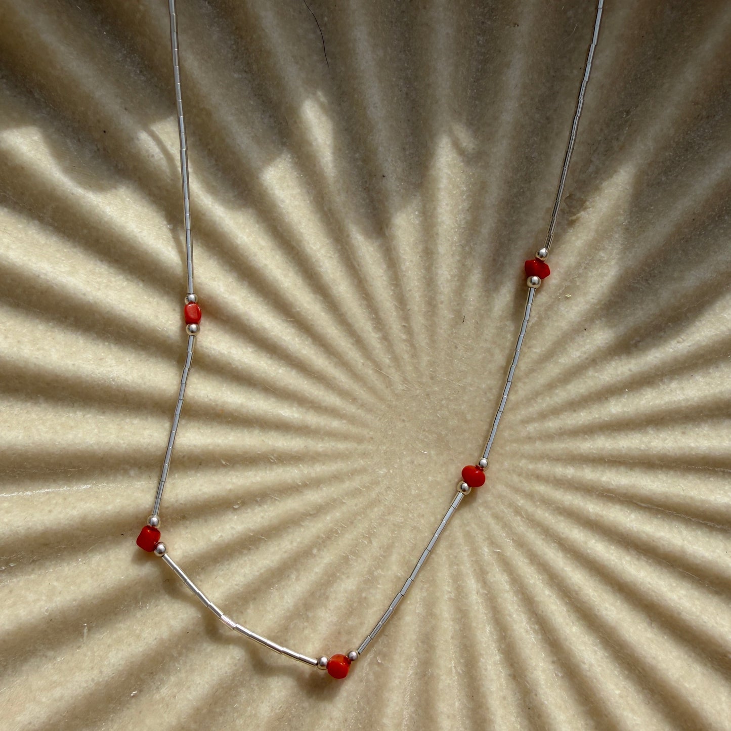 Necklace with red beads on a textured beige surface