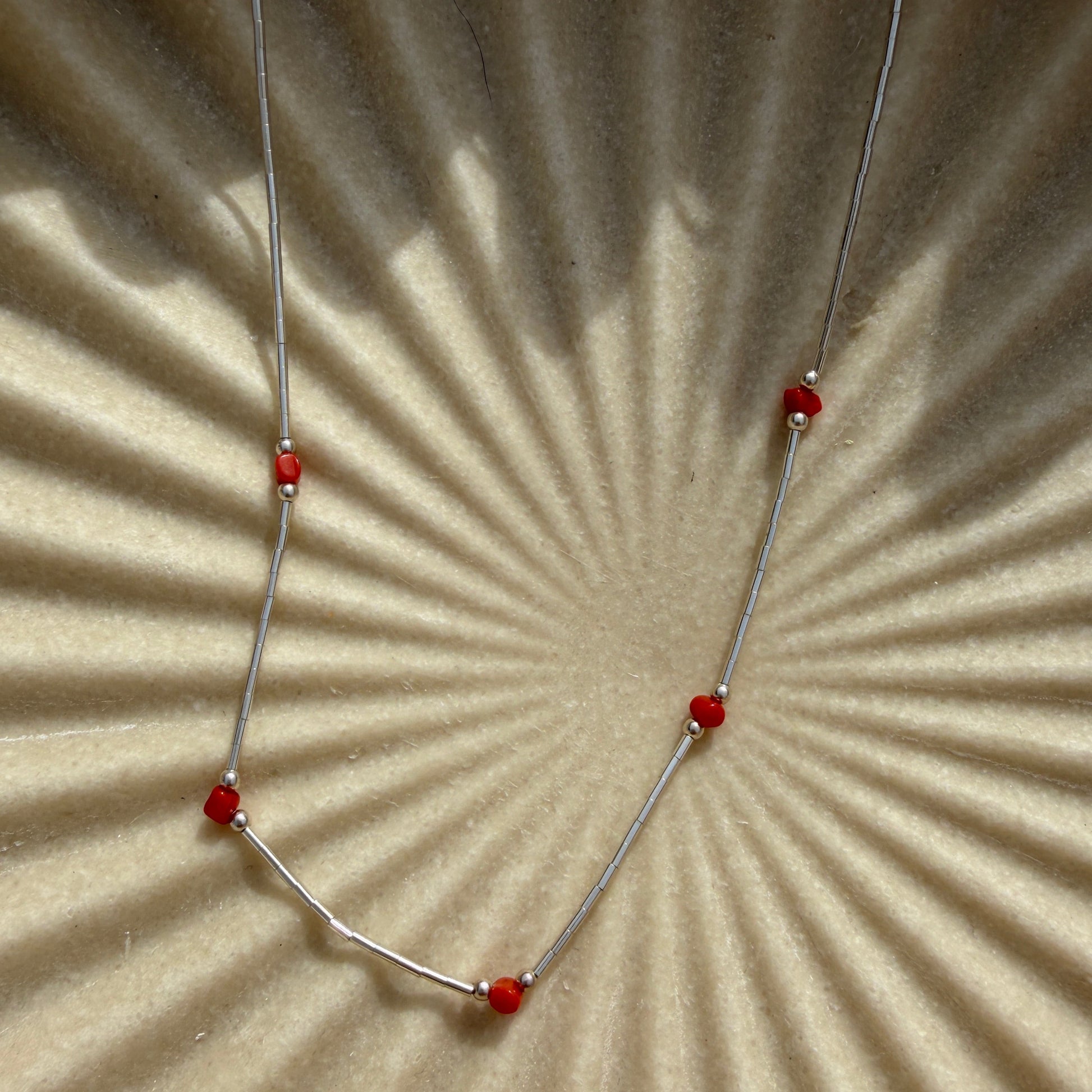 Necklace with red beads on a textured beige surface