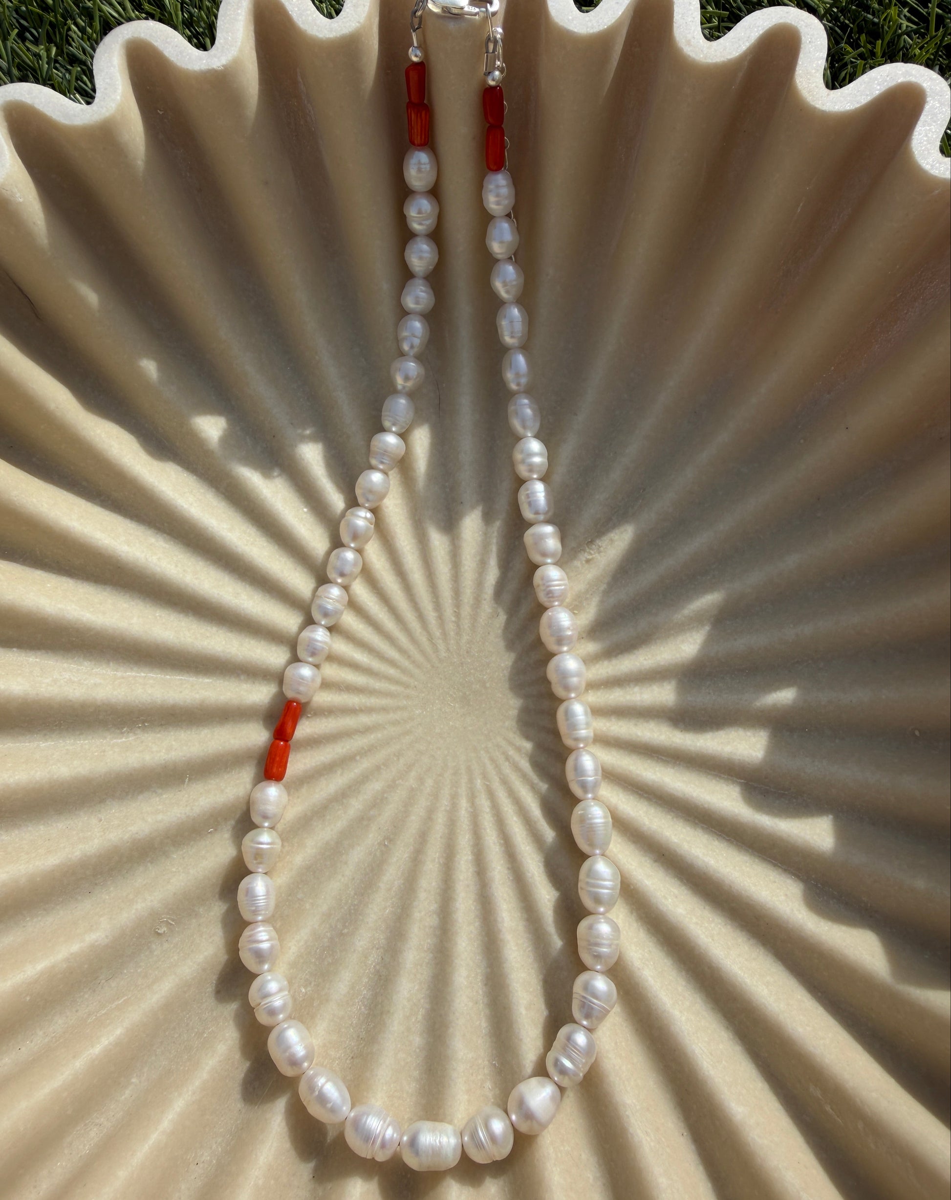 Pearl necklace with coral accents on a textured beige surface