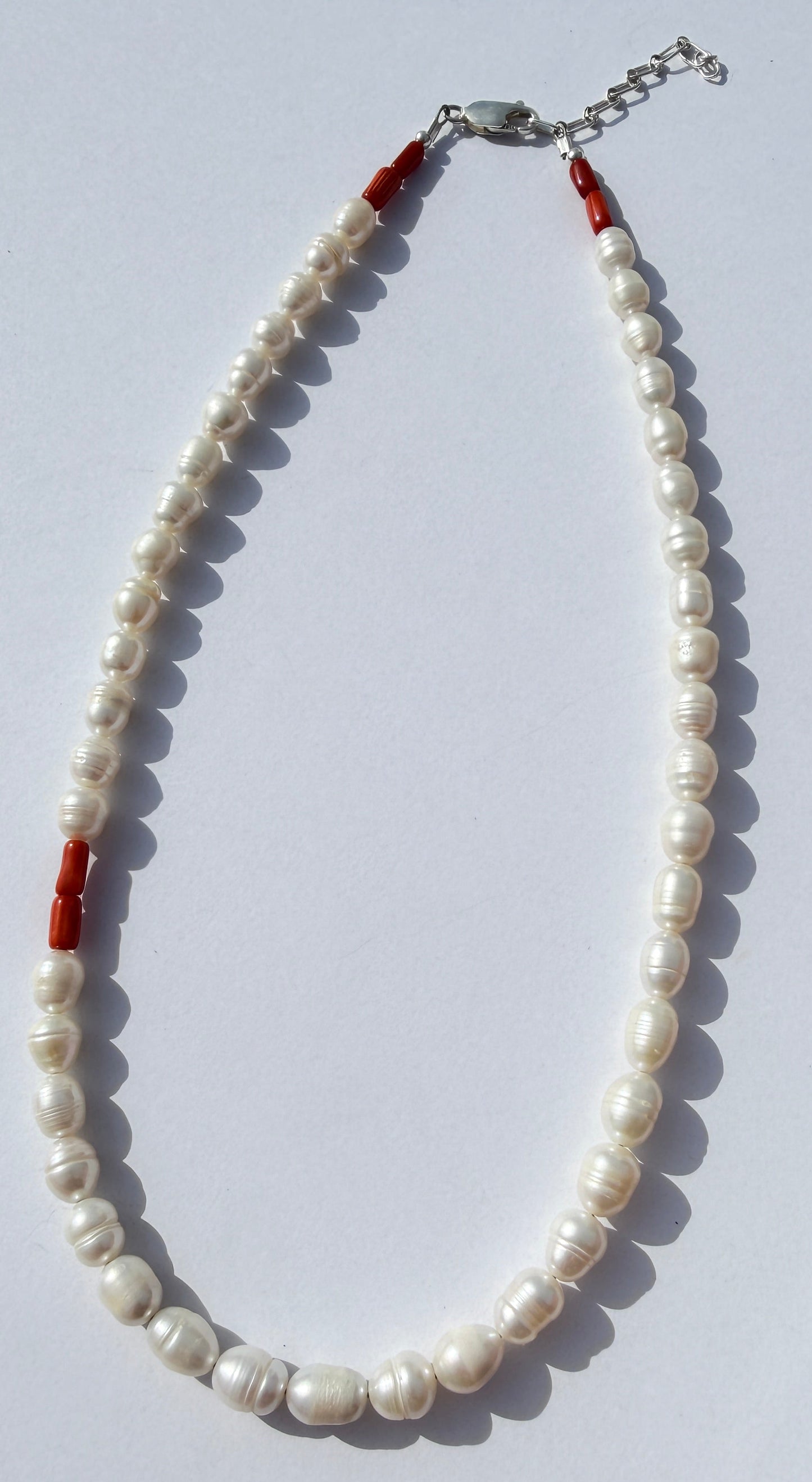 Pearl necklace with red accents on a white surface