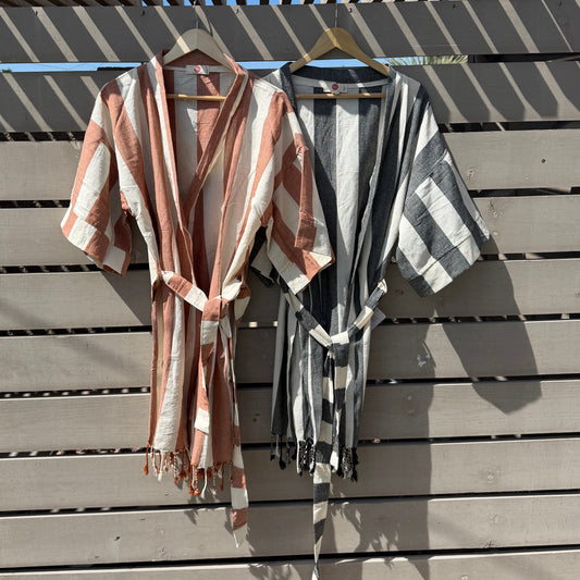 Two striped coverups hanging on a wooden fence with a blue sky background