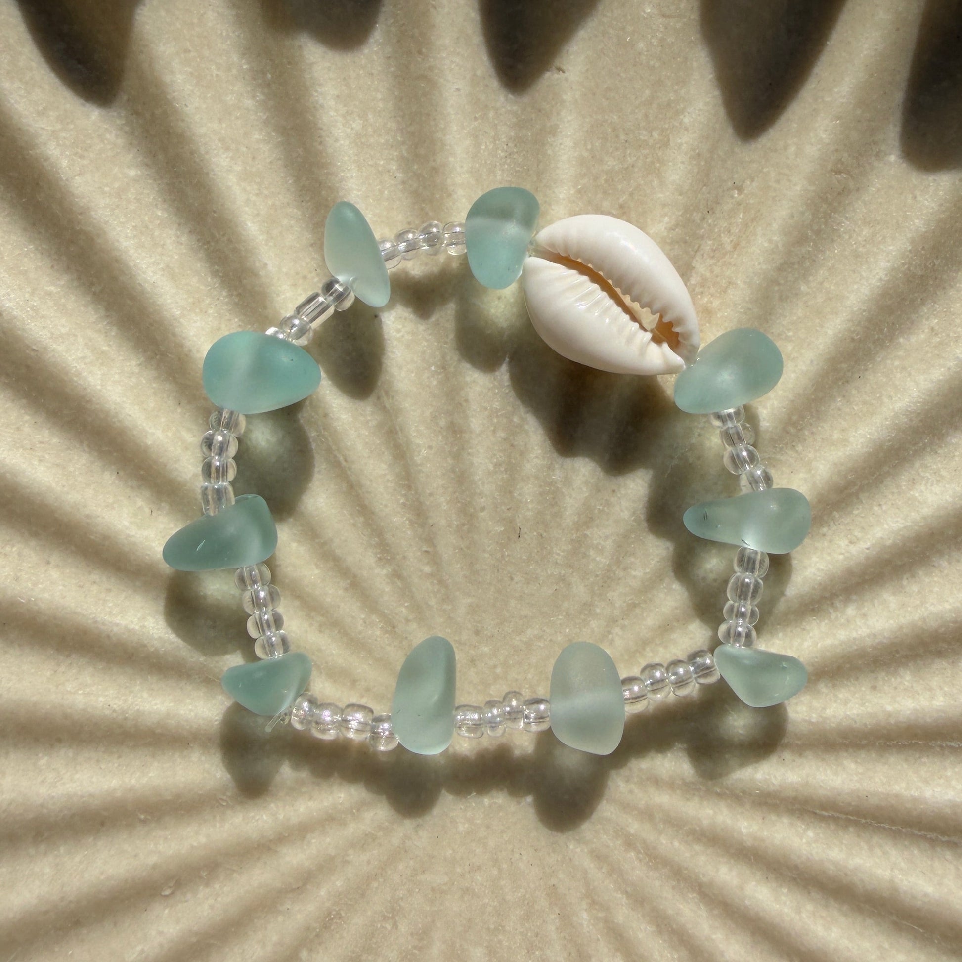 Bracelet with green beads and a shell on a textured beige background