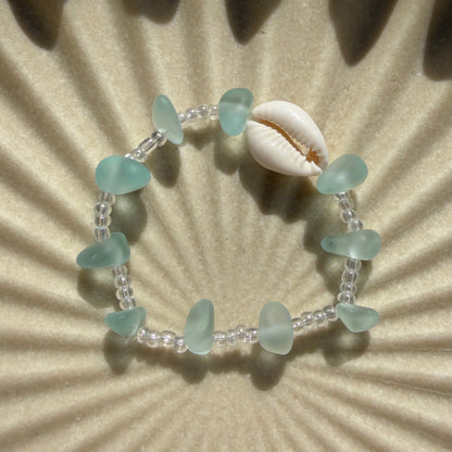 Bracelet with green beads and a shell on a textured beige background