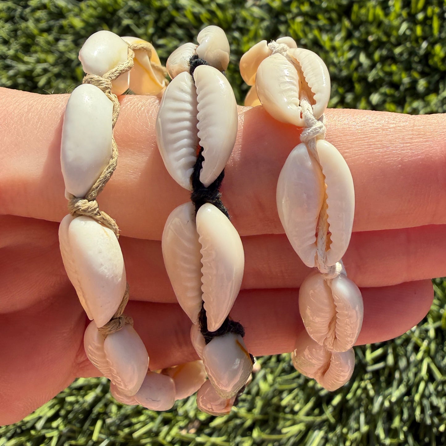 Shell bracelets on a hand with a grassy background