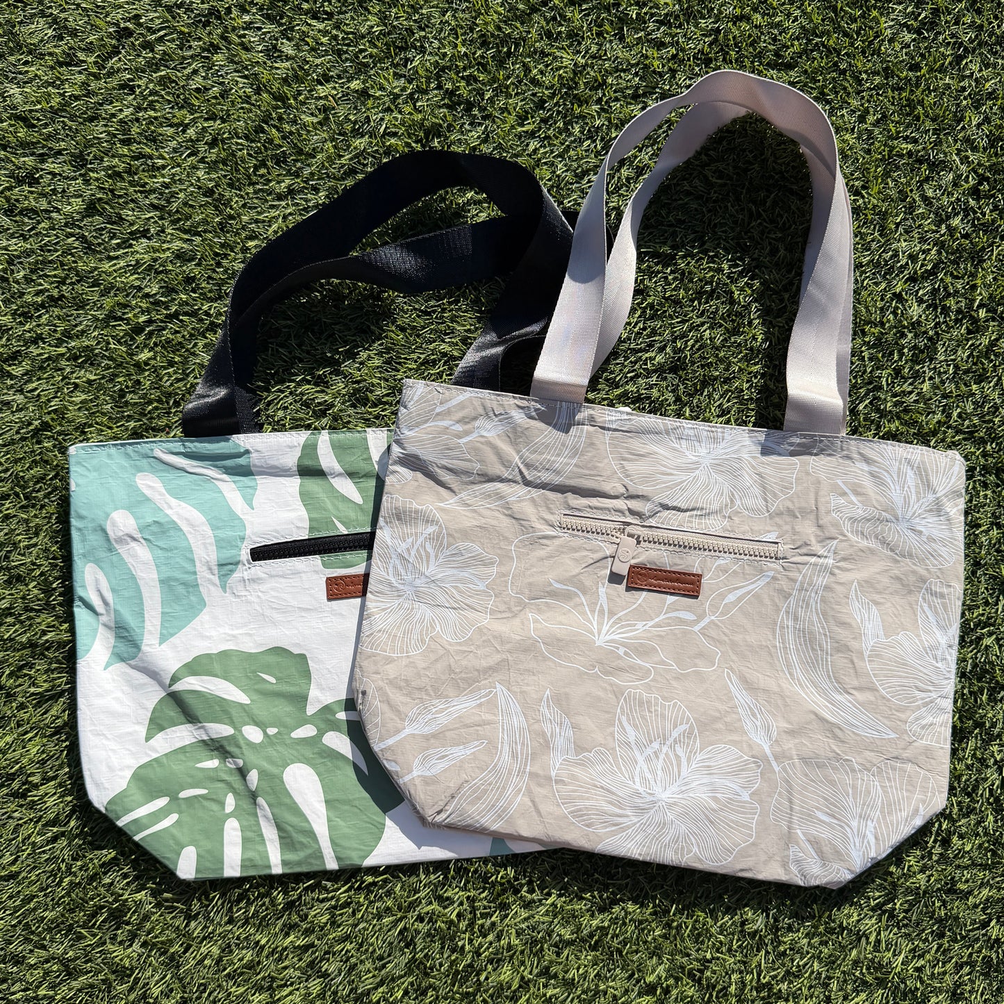 Two handbags on a grassy surface, one with leaf pattern and the other plain.