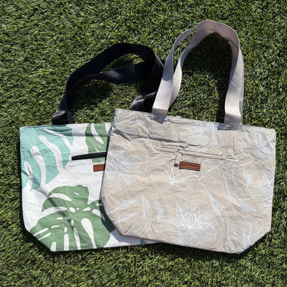 Two handbags on a grassy surface, one with leaf pattern and the other plain.