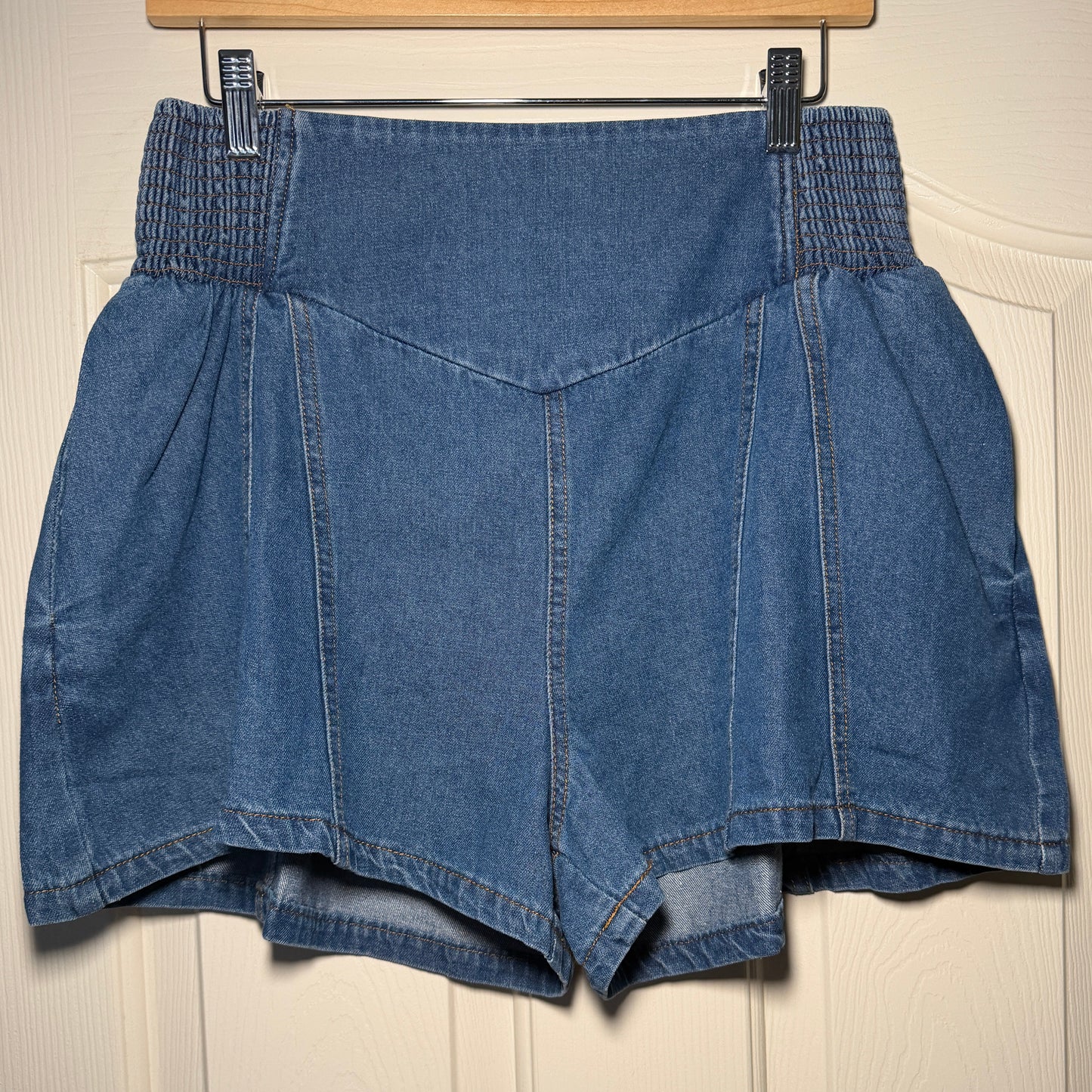Folded blue denim jeans on a wooden hanger against a beige wall.