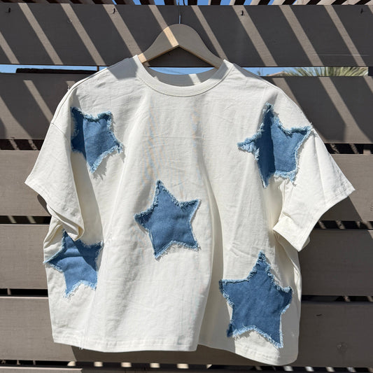White top with blue star patterns hanging on a wooden rack against a blue sky.