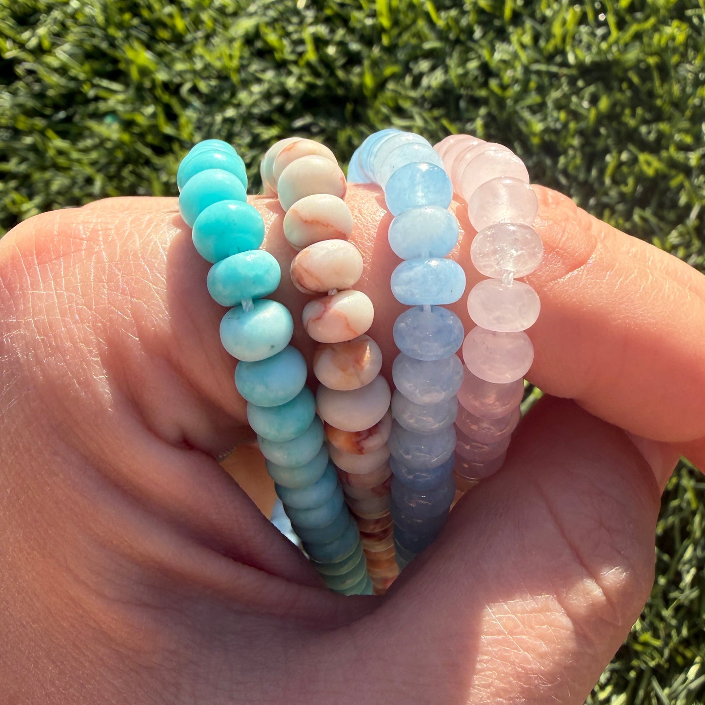 Hand holding a stack of colorful beaded bracelets against a grass background