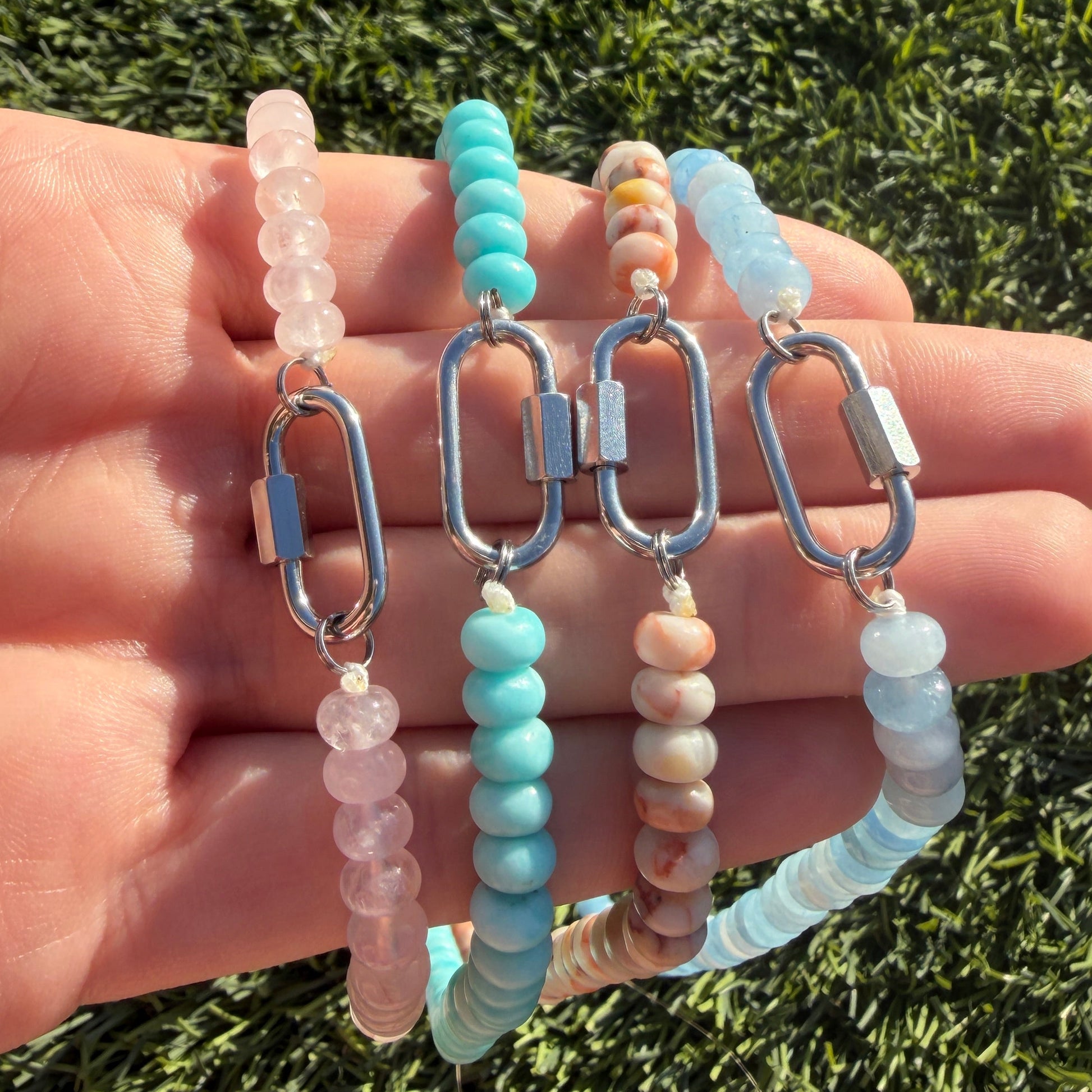 Hand holding multiple beaded necklaces against a grass background