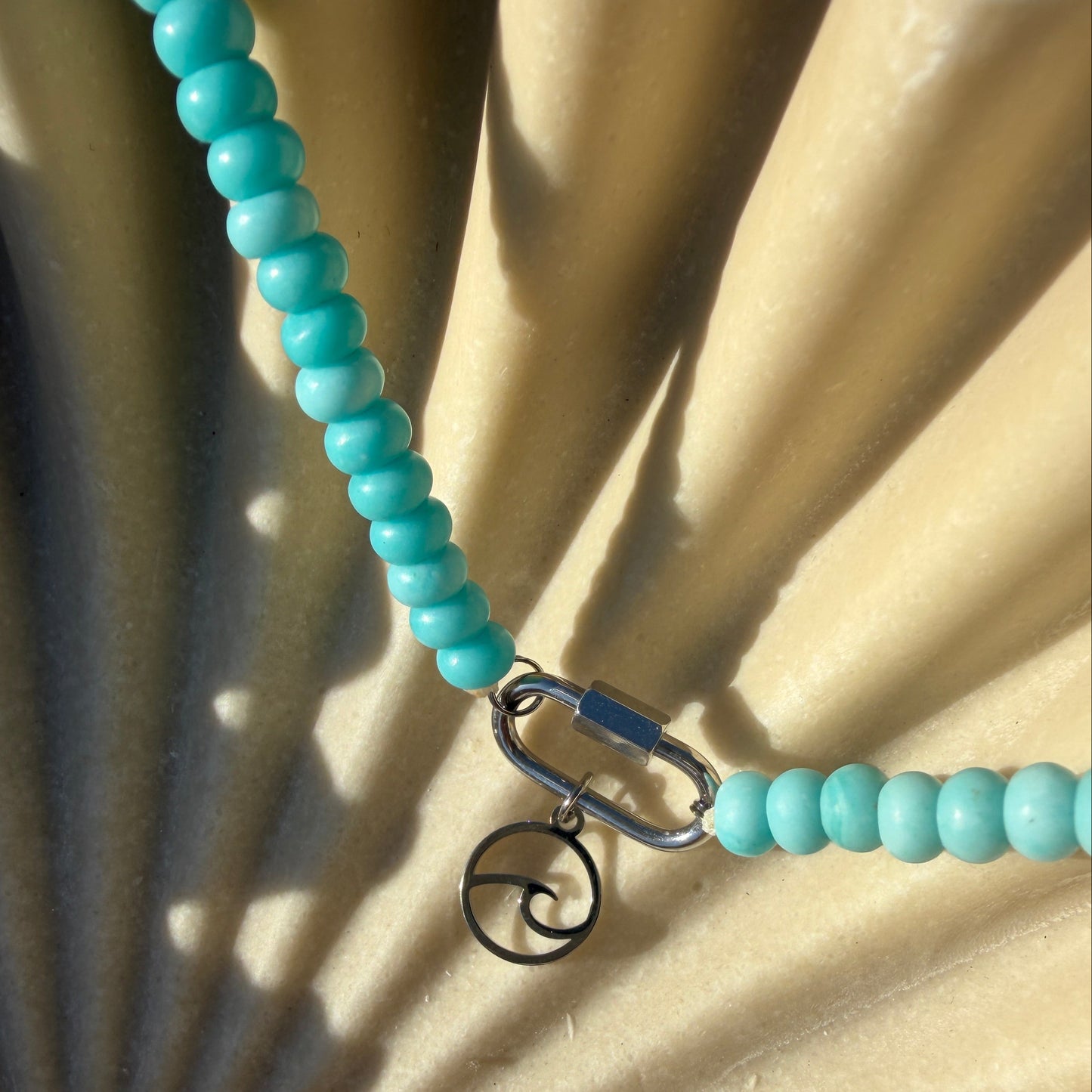 Turquoise beaded necklace with a metal clasp on a textured beige surface