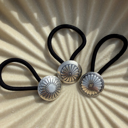 Three black hair ties with silver floral ends on a beige background