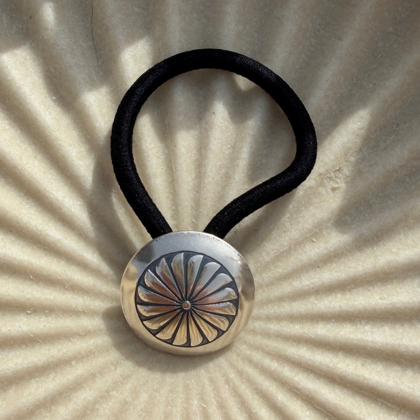 Hair tie with a metallic button on a textured beige background