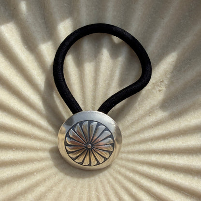 Hair tie with a metallic button on a textured beige background