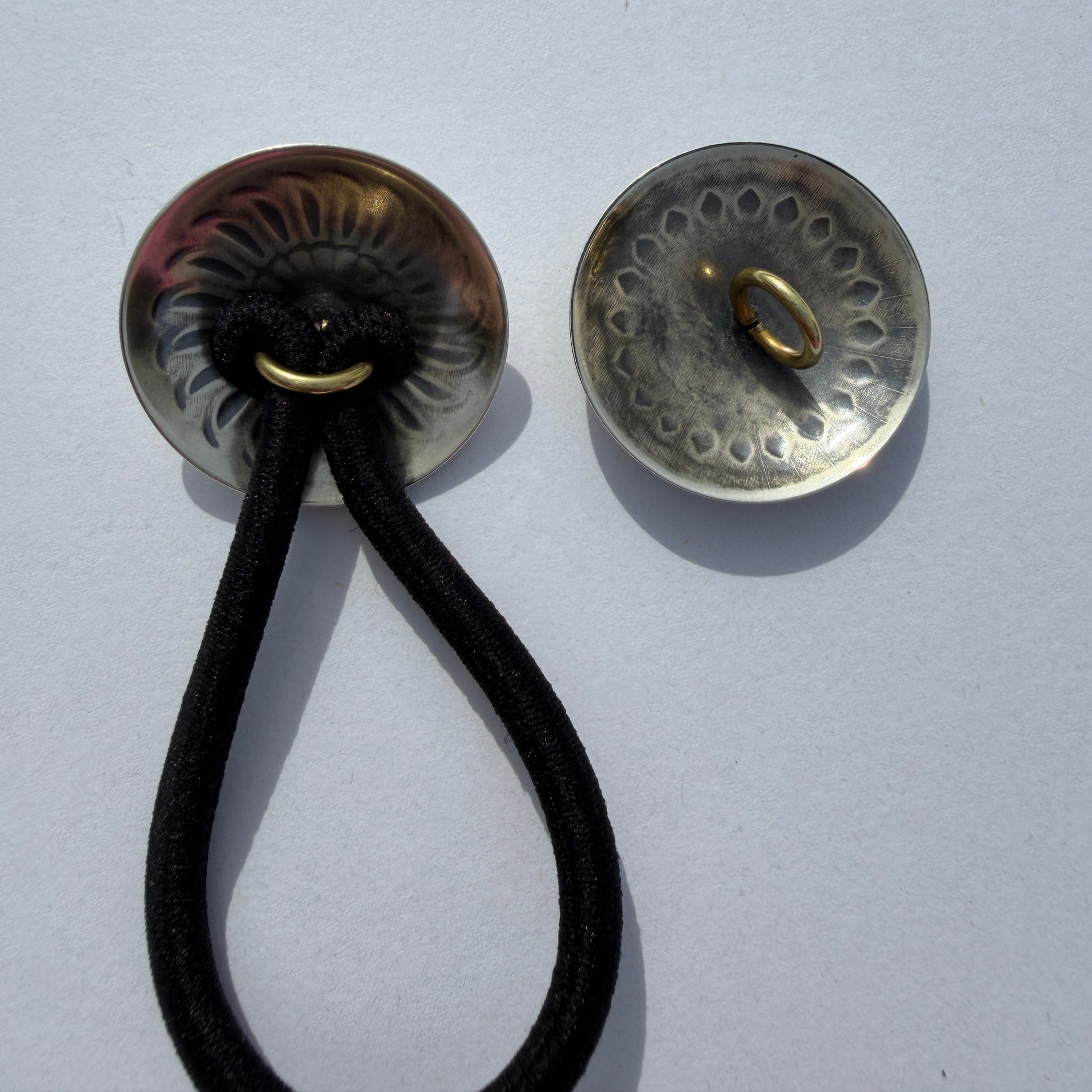 Two metallic buttons with a black cord on a light gray background