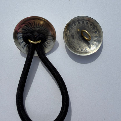 Two metallic buttons with a black cord on a light gray background