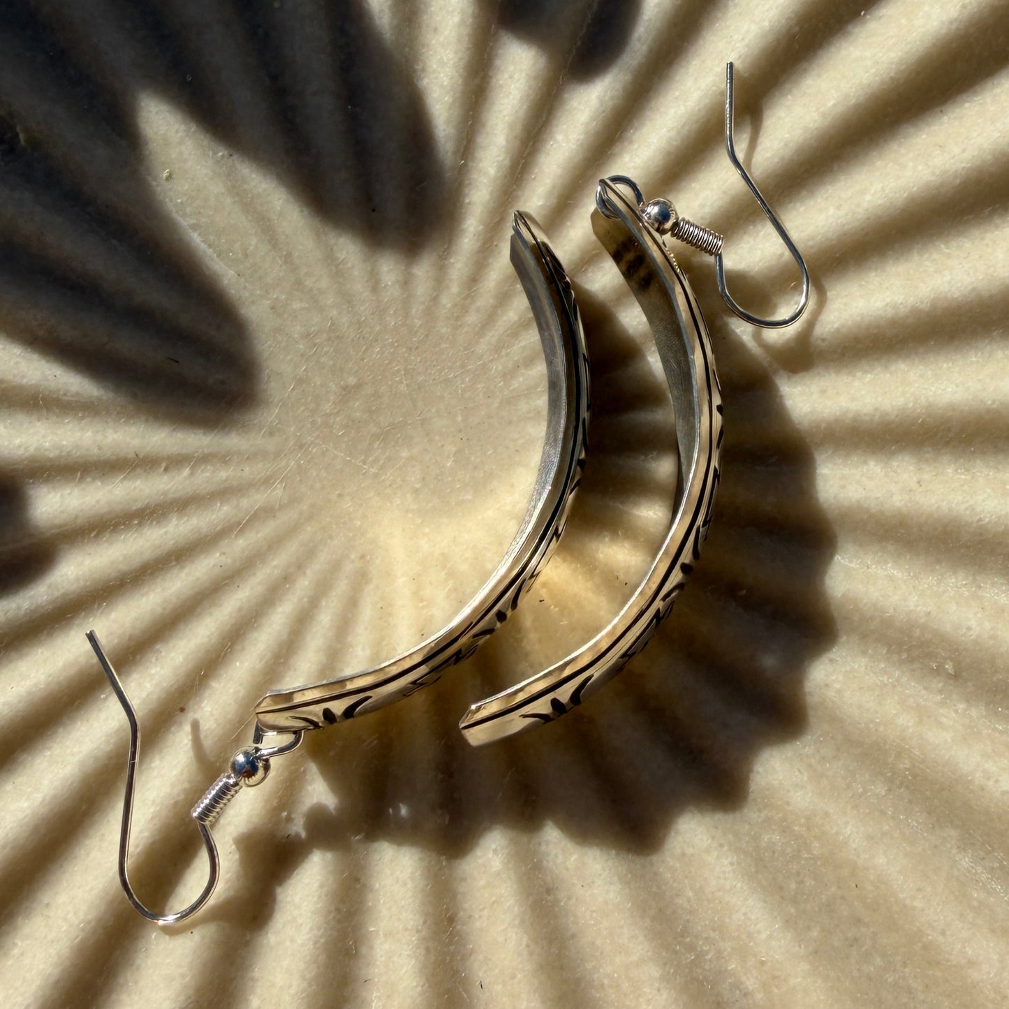 Silver half hoop dangle earrings on a textured surface