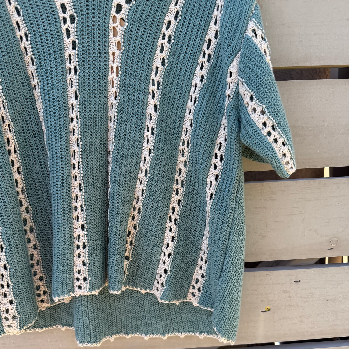 Teal and white crochet top draped over a wooden surface