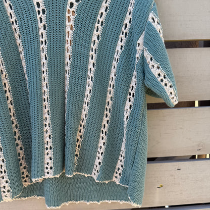 Teal and white crochet top draped over a wooden surface