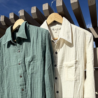 Two shirts, one green and one beige, hanging on wooden hangers against a blue sky.