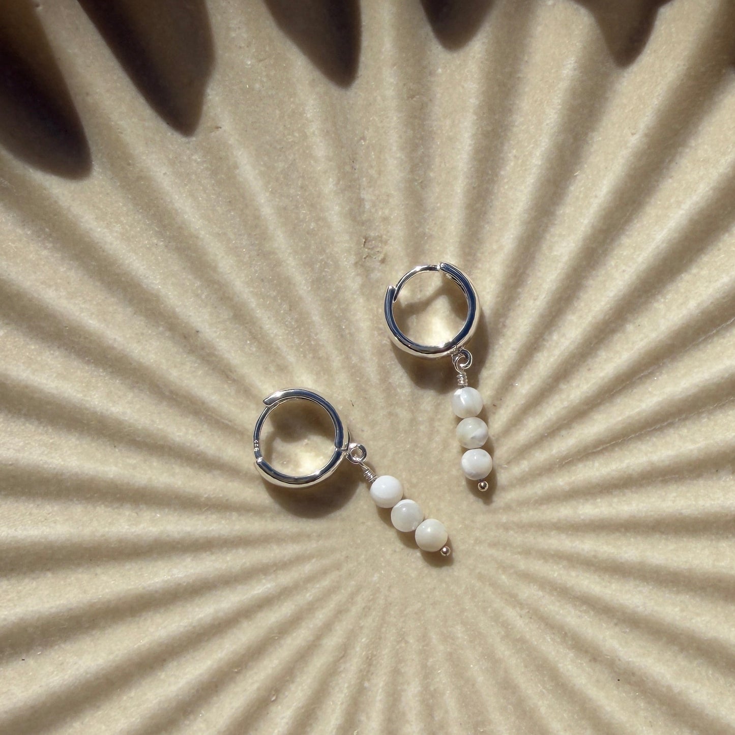 Pair of silver earrings on a textured beige surface with sunburst pattern