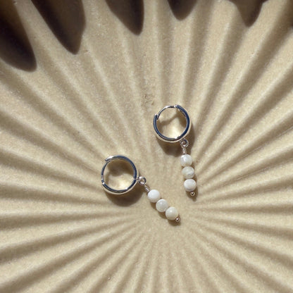 Pair of silver earrings on a textured beige surface with sunburst pattern