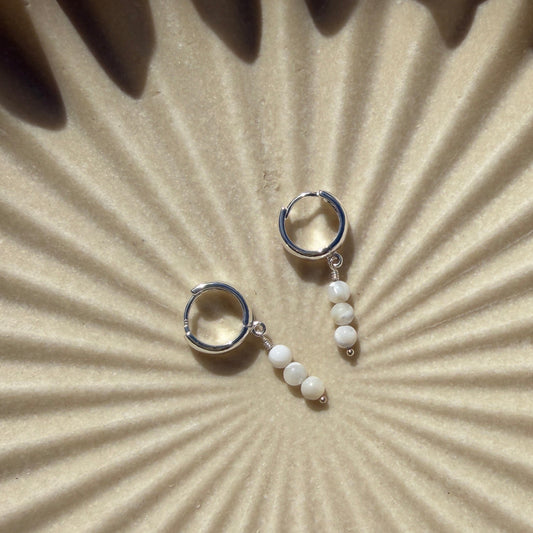 Pair of silver earrings on a textured beige surface with sunburst pattern