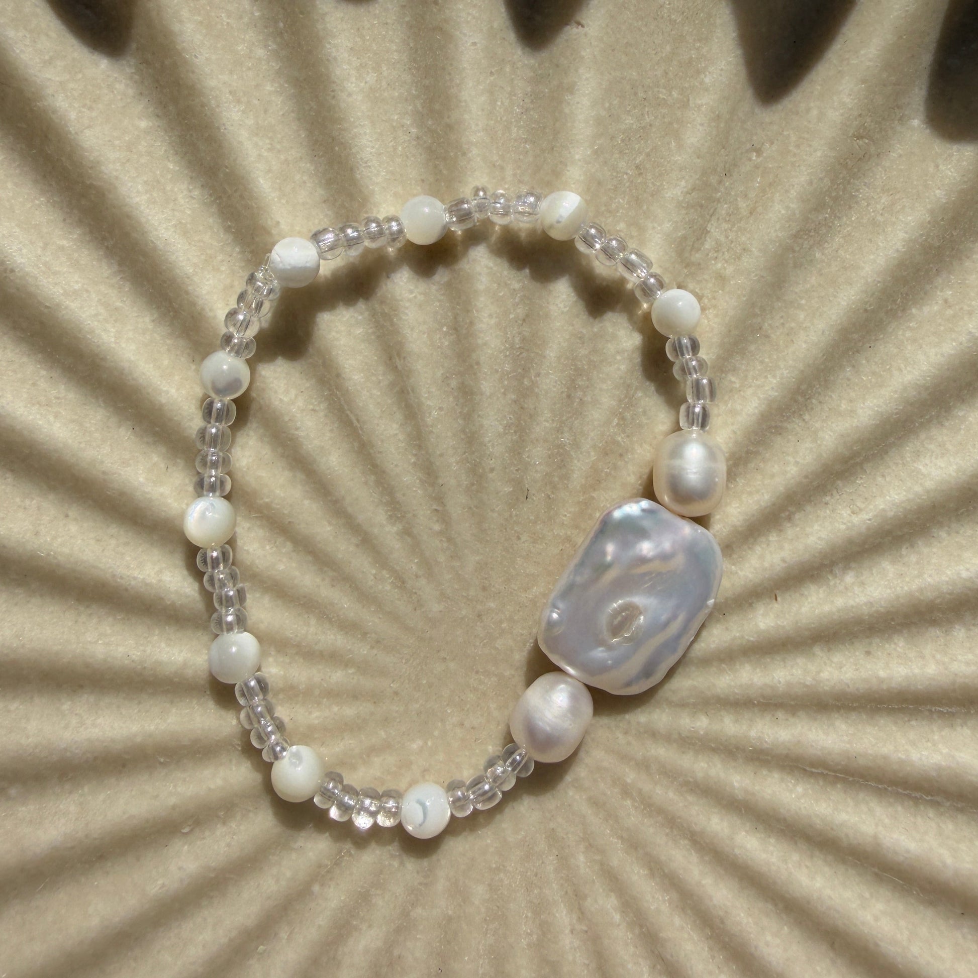 Pearl bracelet with a central stone on a textured beige background