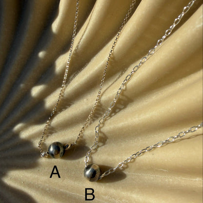 Two silver necklaces with small pendants on a beige surface.