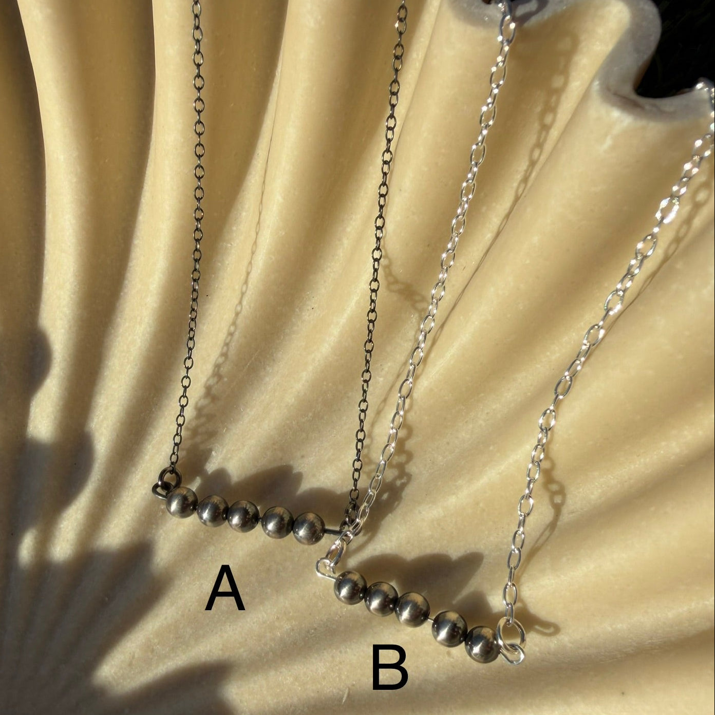 Two necklaces on a textured beige surface with a sunburst pattern