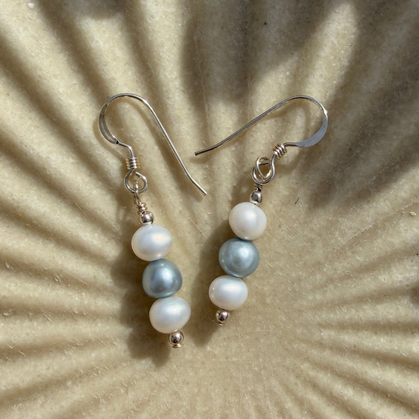 Pair of pearl earrings on a textured beige surface with sunlight casting shadows.