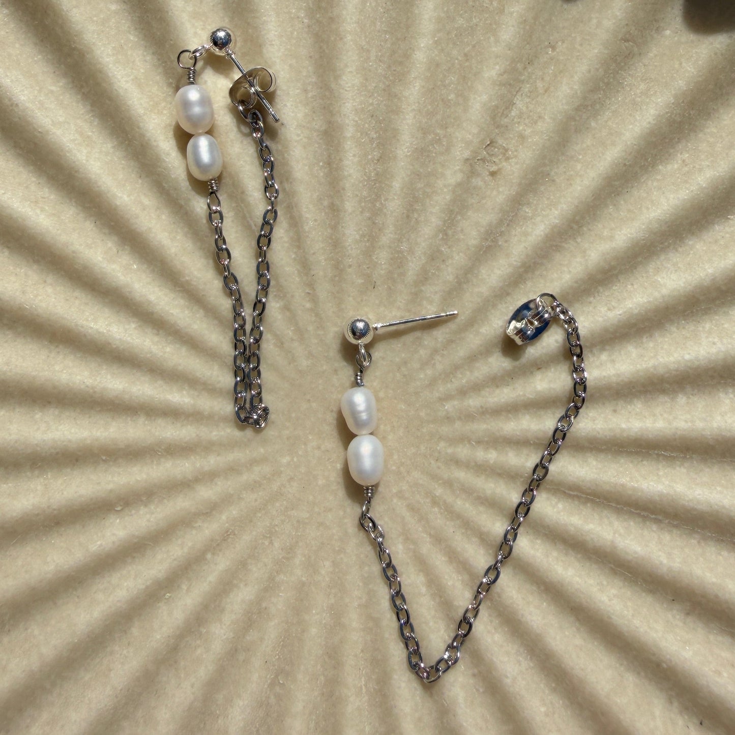 Pearl earrings on a textured beige surface with a sunburst pattern