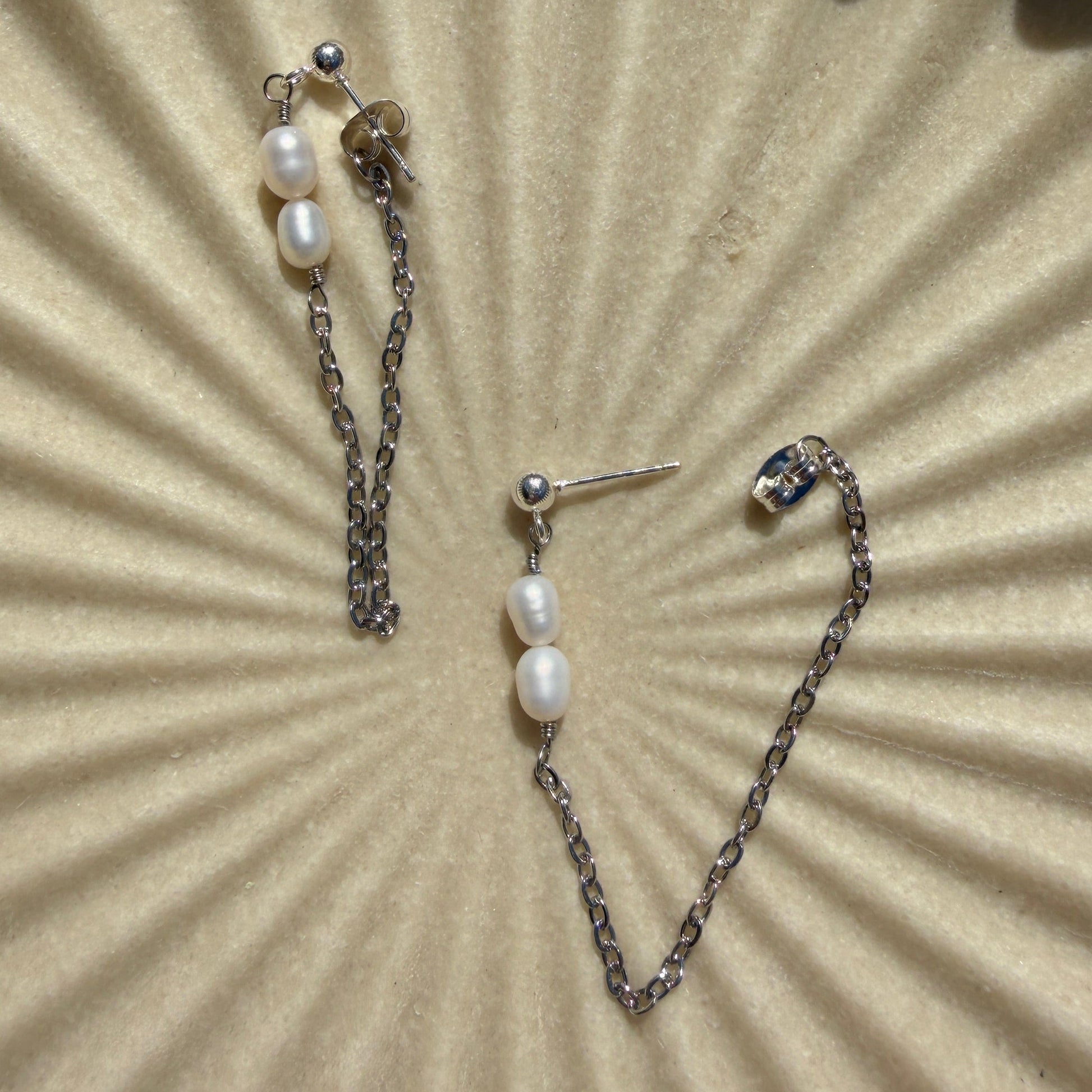 Pearl earrings on a textured beige surface with a sunburst pattern