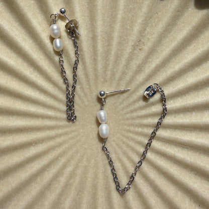 Pearl earrings on a textured beige surface with a sunburst pattern